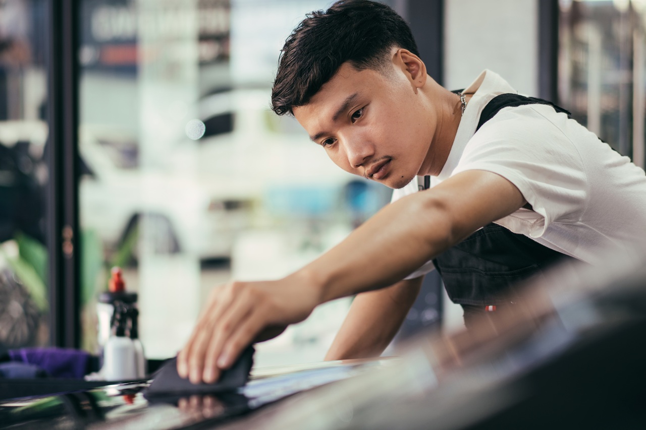 Asian detailing film paint protection men specialist cleaning and wrapping car in garage showroom, protective coating installation and polishing automobile for vehicle care service business concept