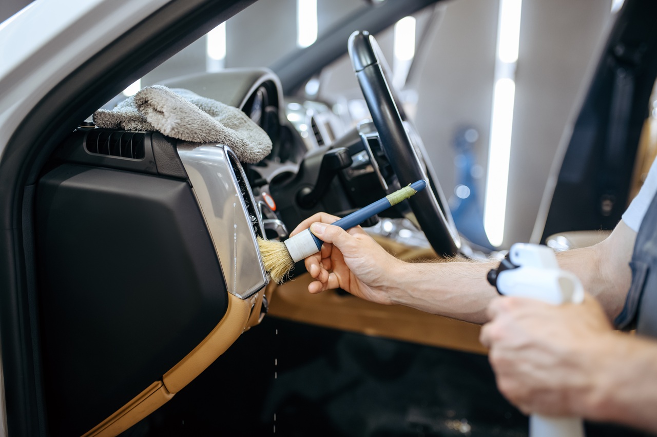 Worker with brush wipes car air duct grating, dry cleaning and detailing. Vehicle washing in garage, thoroughly care of automobile, chemical and vacuum clean service