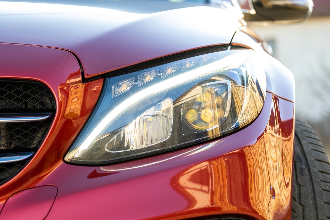 Closeup of front headlight of new clean car parked on a city street side.